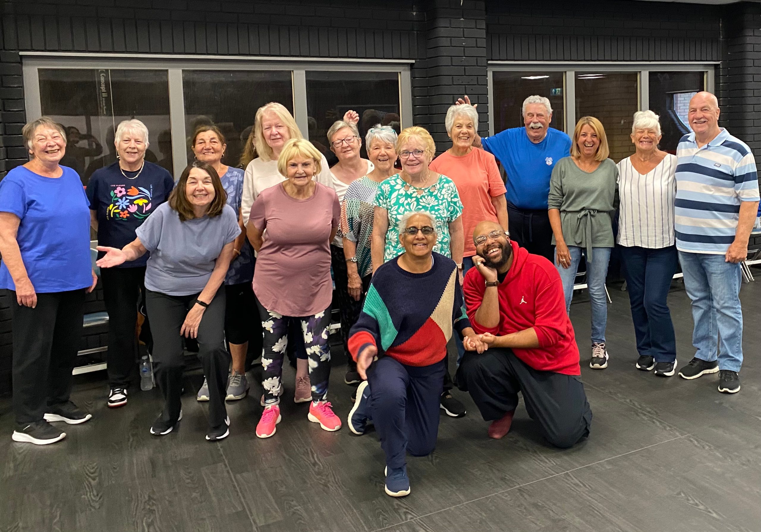 A large group of mostly older adults are posing and smiling for a group photo in a room.