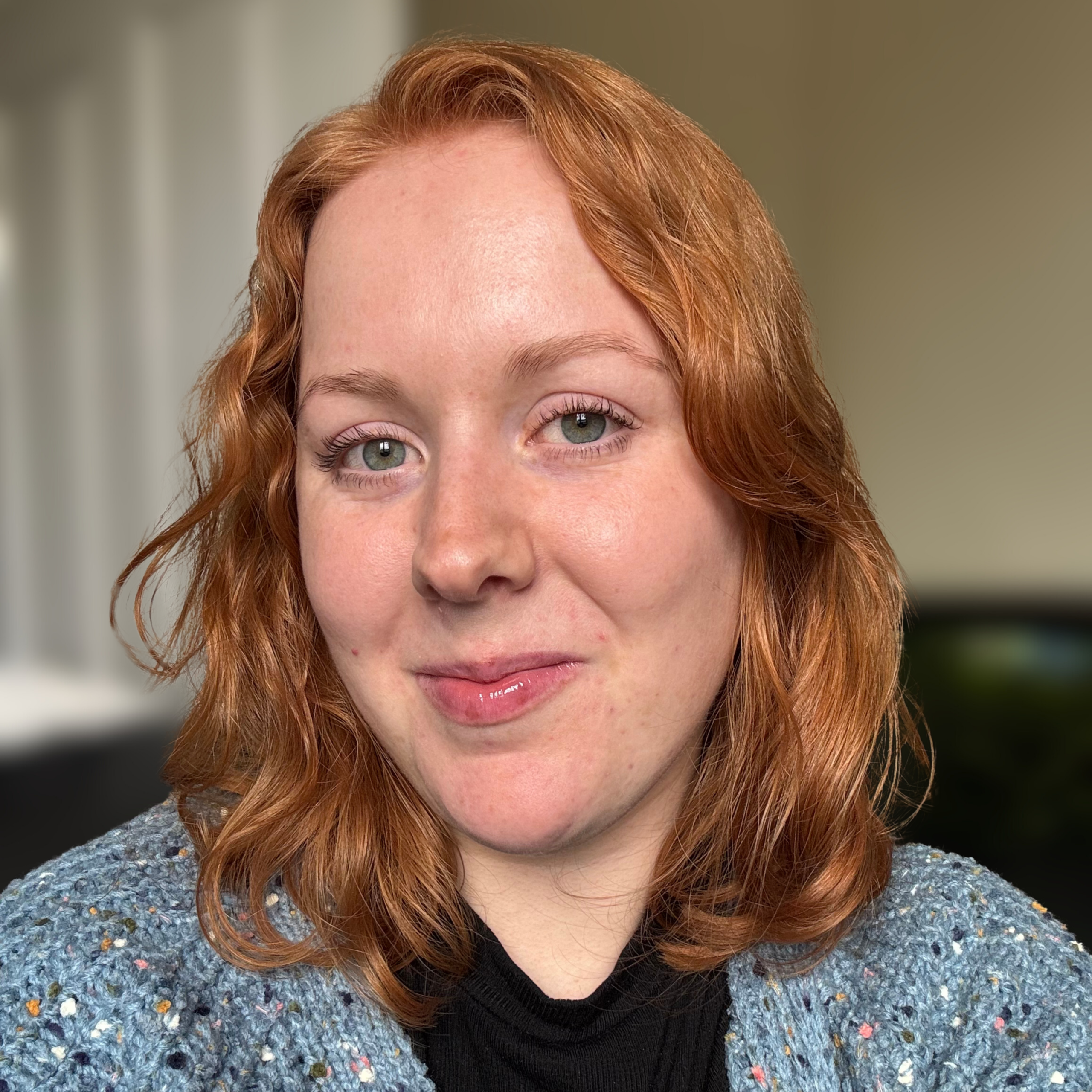 Portrait of a smiling red-haired woman wearing a blue knitted cardigan.